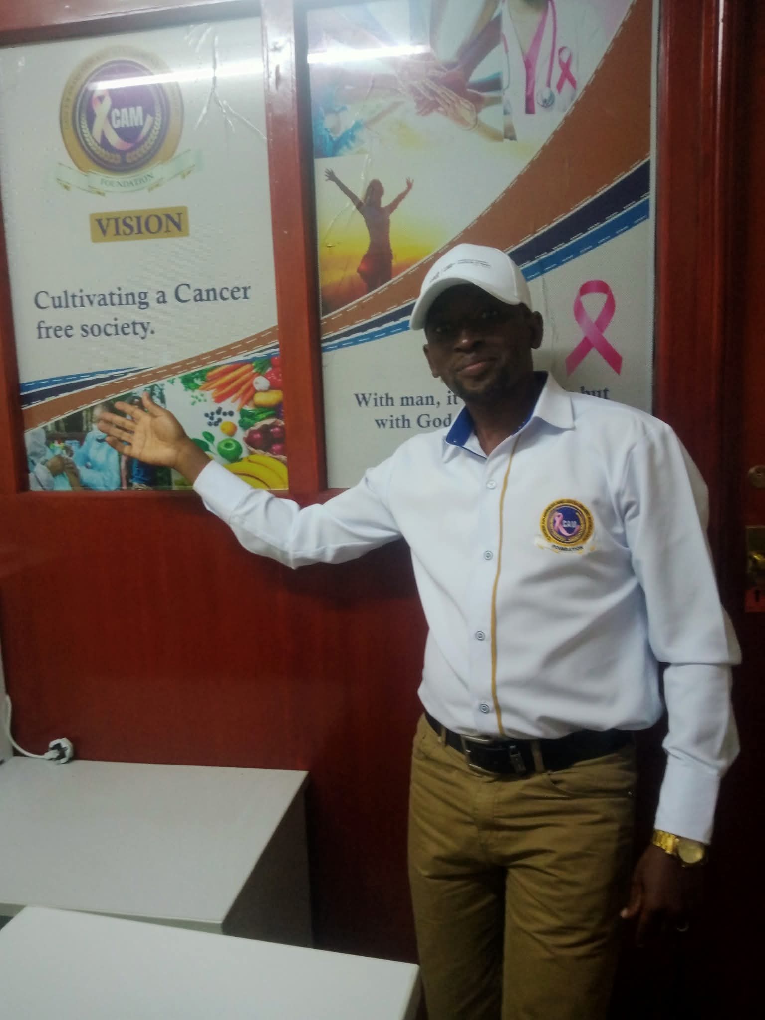CAM Foundation founder at the organization's office, beside the vision statement: cultivating a cancer-free society.